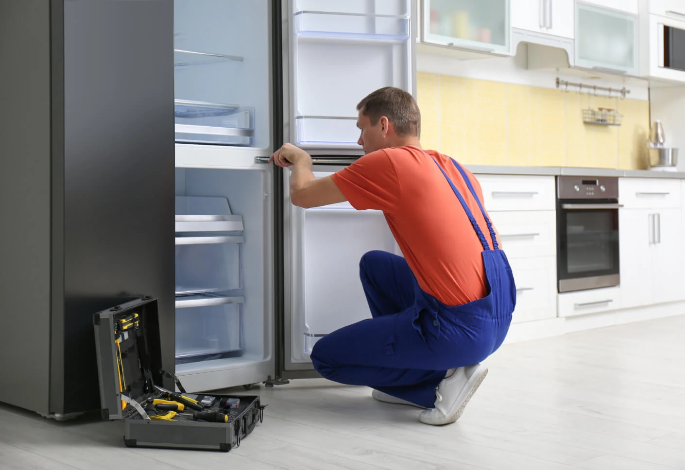 Technician in orange workwear inspecting an open refrigerator in a residential kitchen